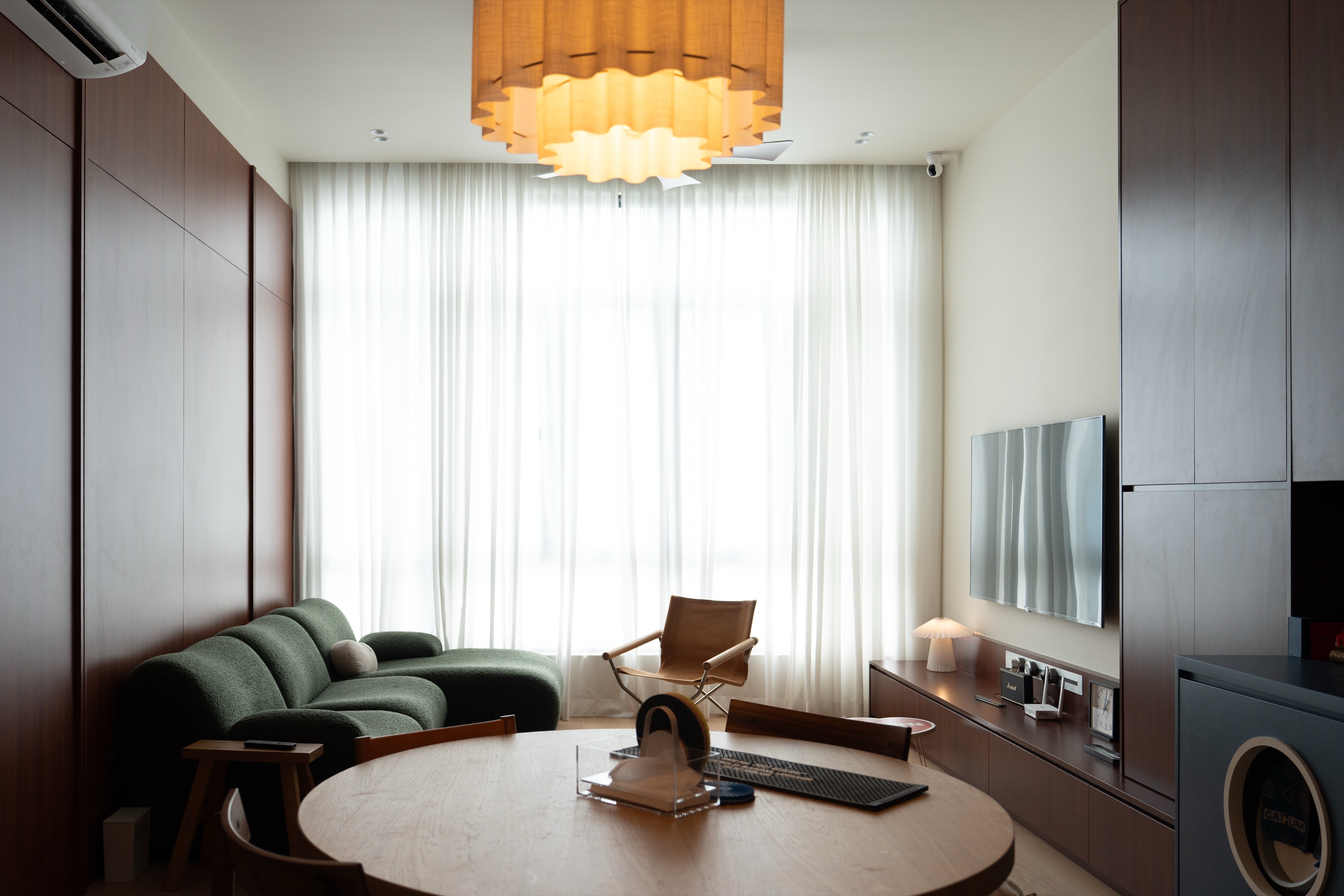 Living room with full-height cherry laminate panel wall, floating TV console and round dining table, The Maple OUG