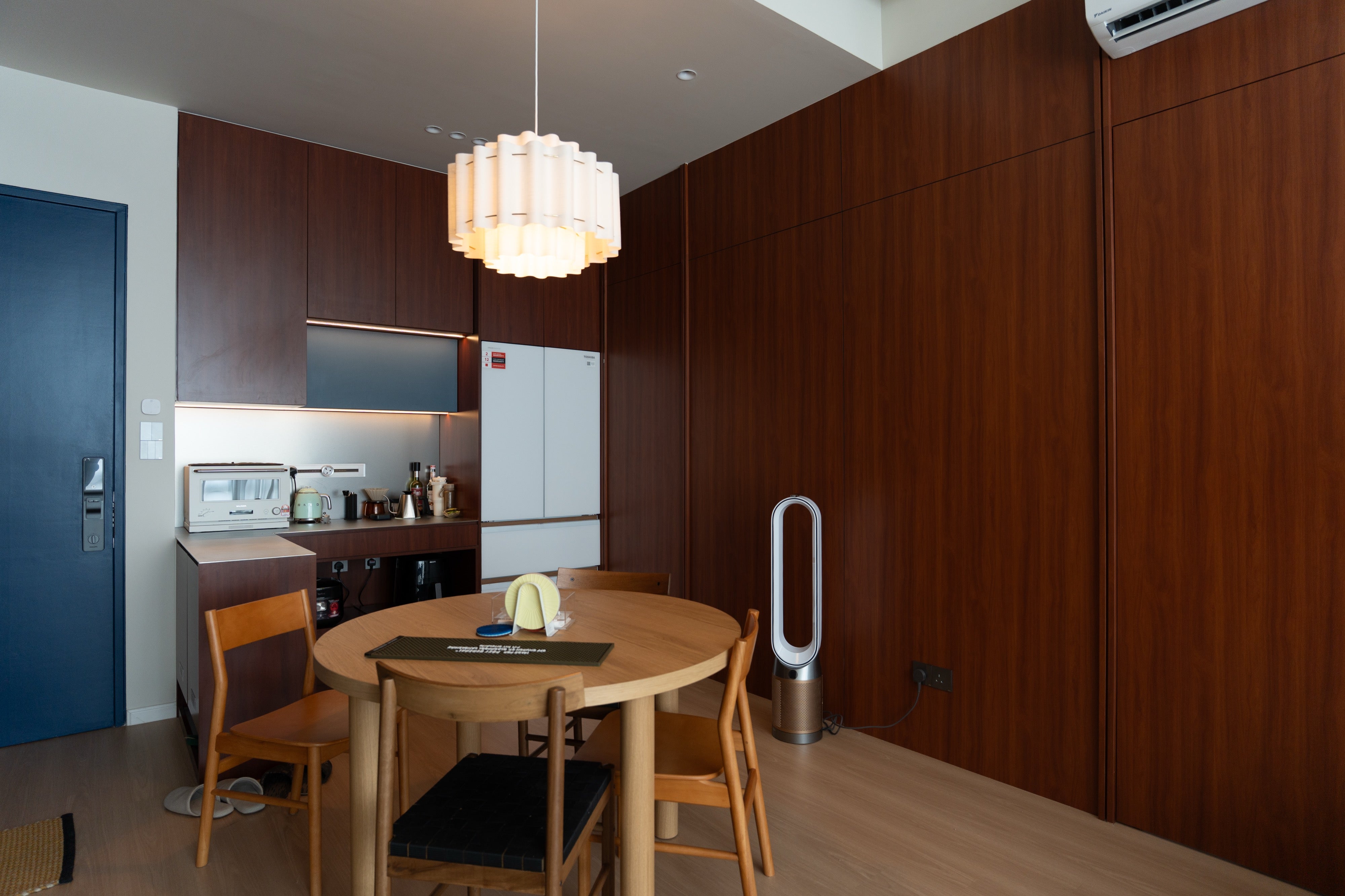 Round dining table under a pleated pendant with the pantry and full-height cherry wall behind