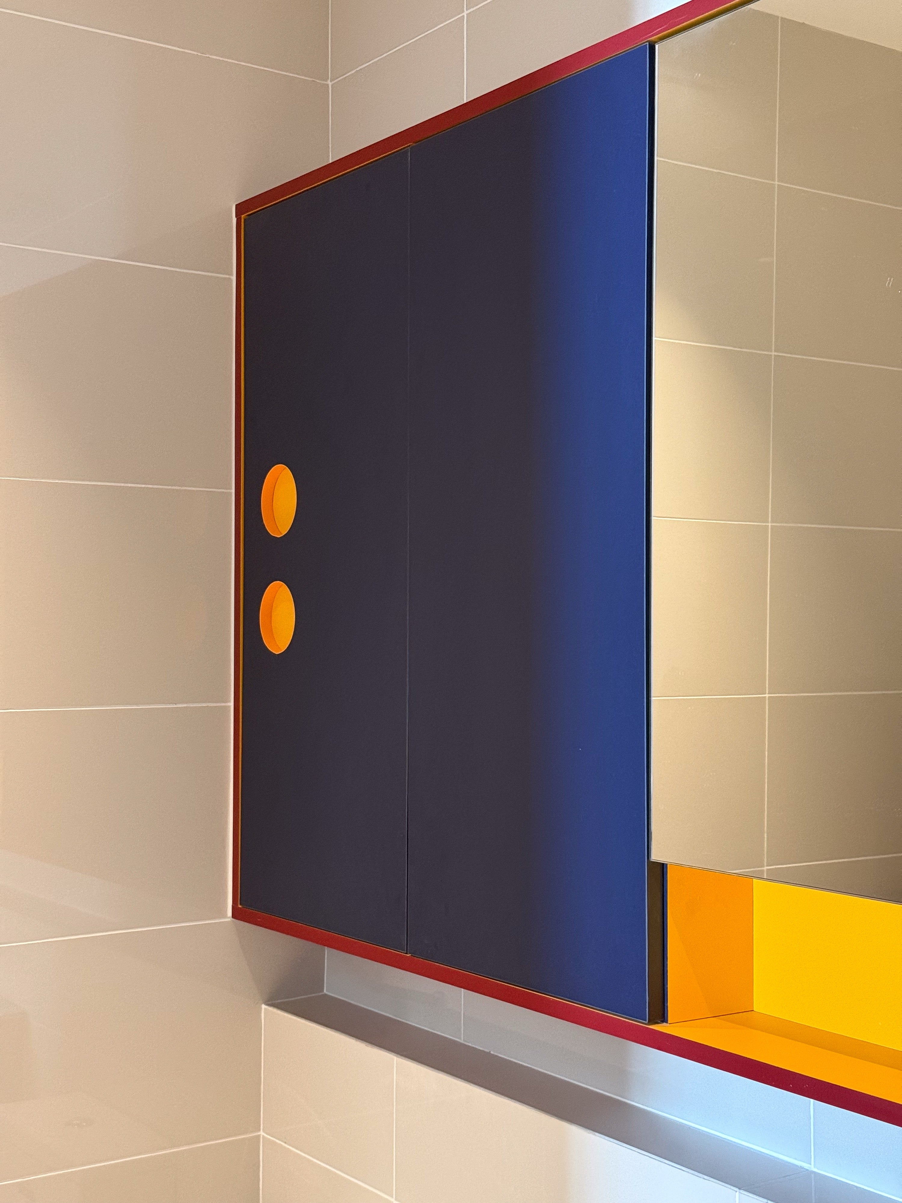Bathroom mirror cabinet in navy with mustard interior and round cut-out handles