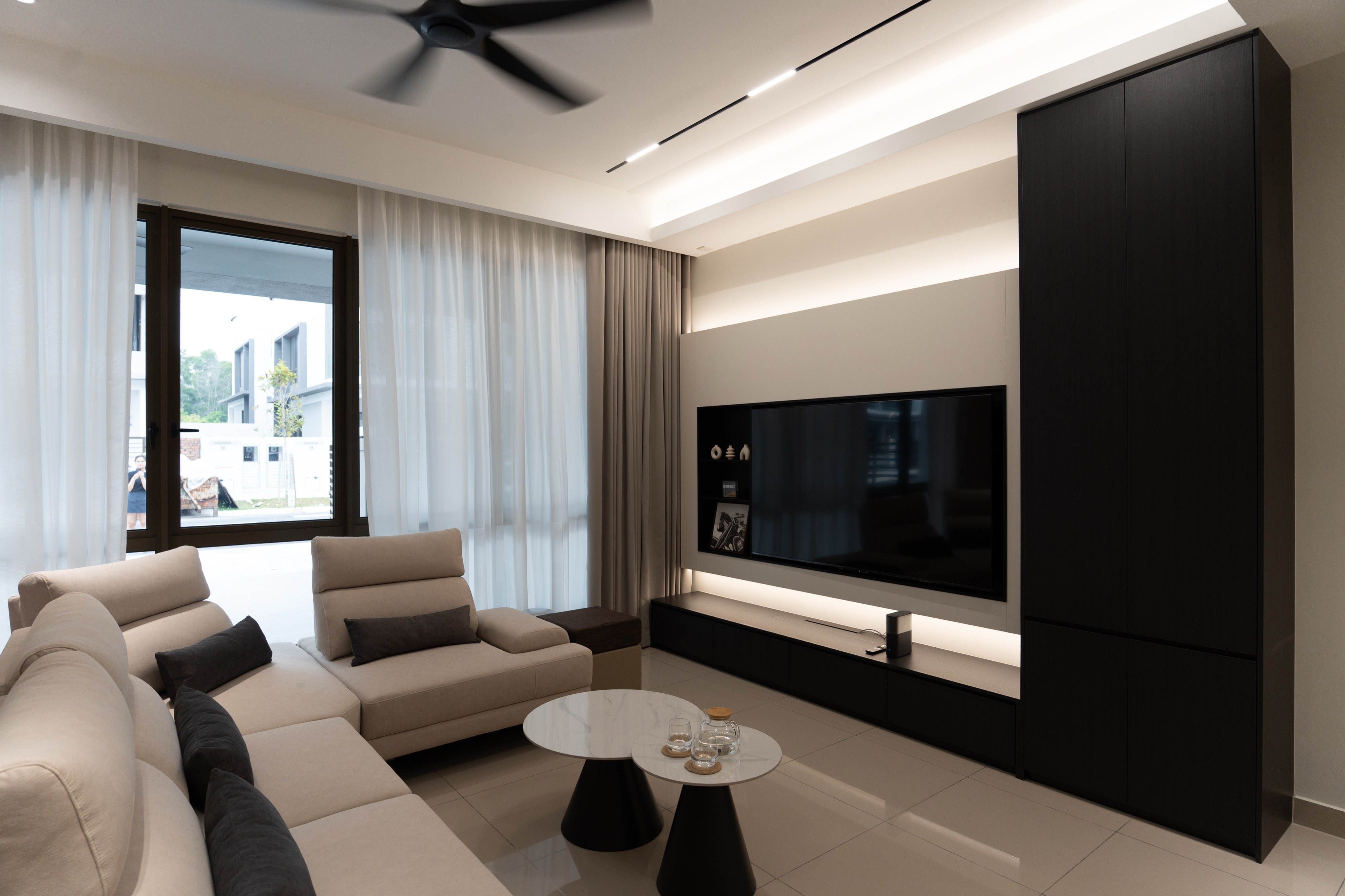 Living room of a landed home at Dahlia Bukit Puchong with cove ceiling, beige TV wall and garden view, interior design by Mugo Space