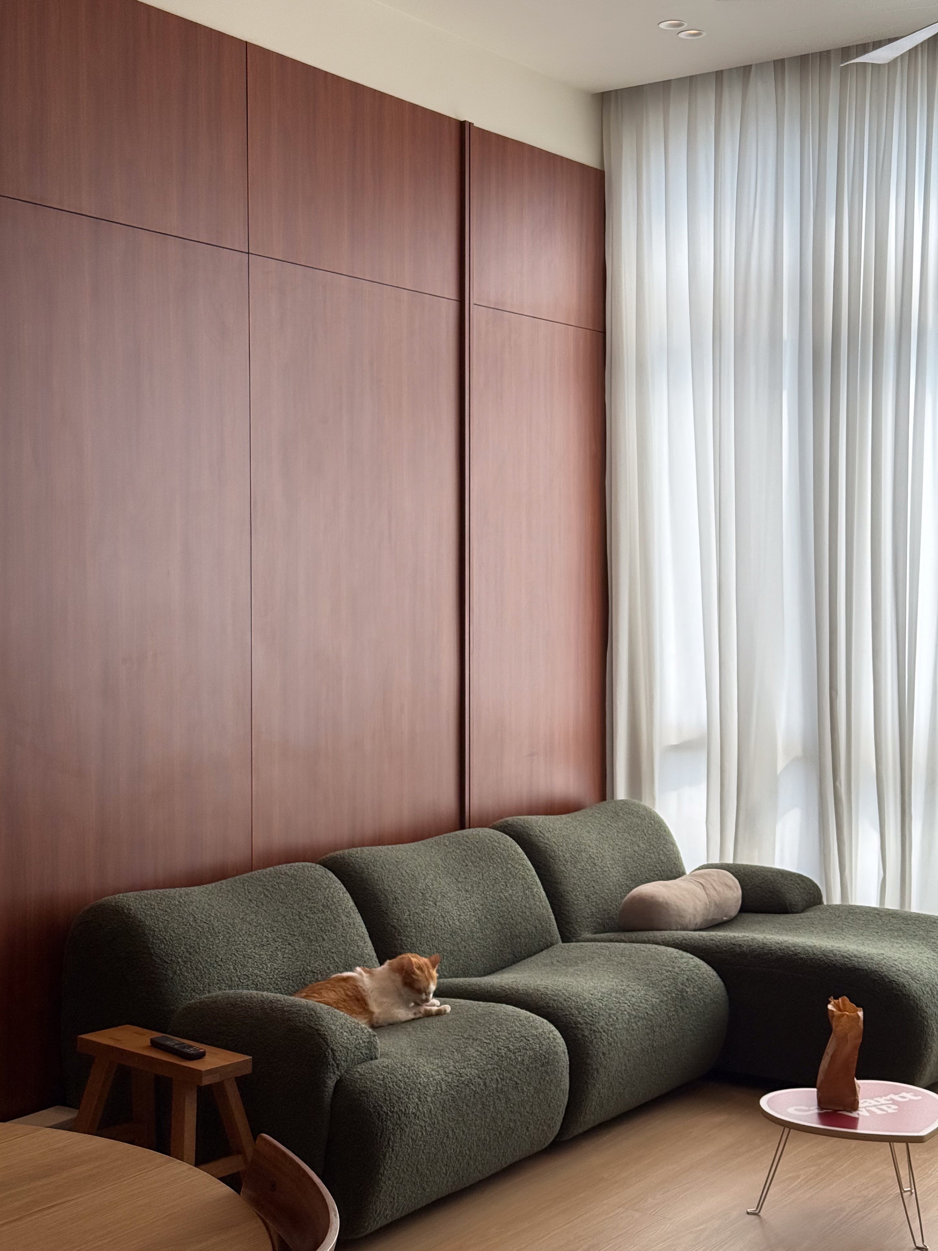 Cherry laminate panel wall behind an olive green boucle sofa with a cat, The Maple OUG