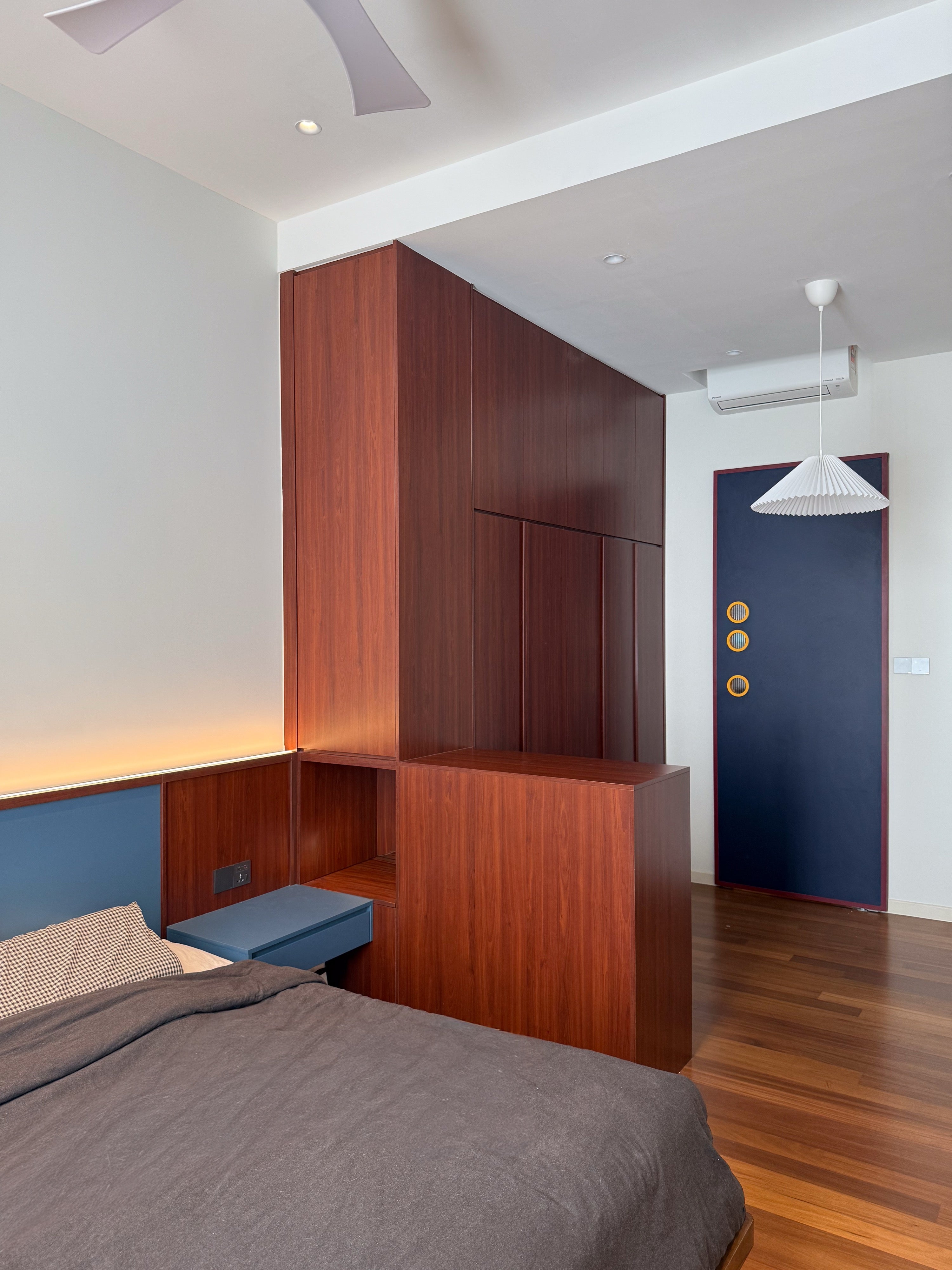 Cherry wardrobe partition behind the bed with floating navy bedside drawer and porthole door